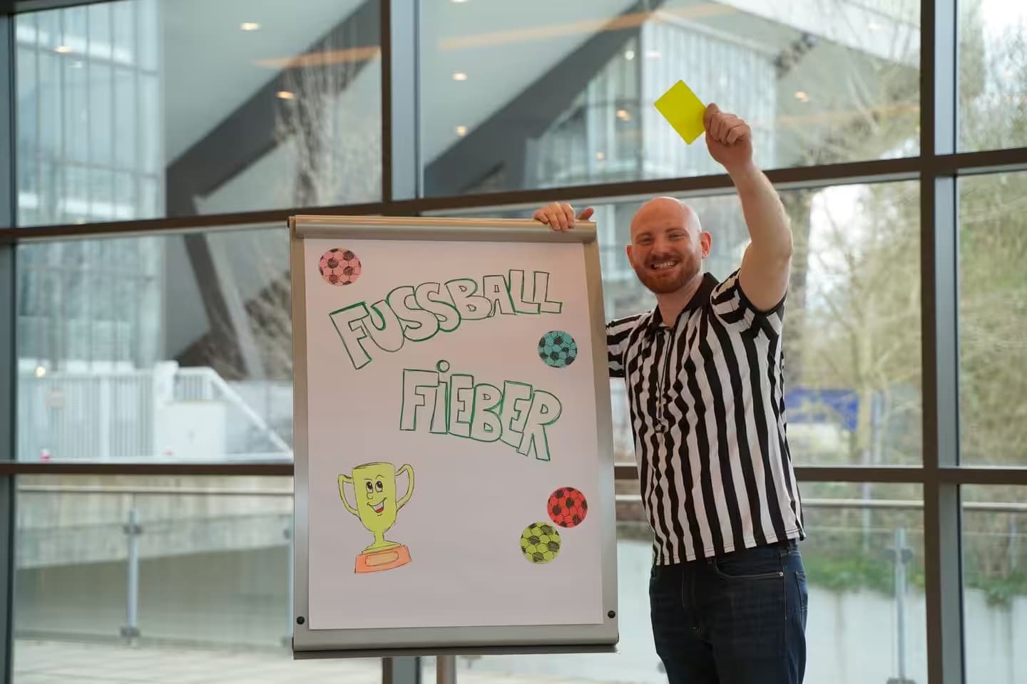 Schiedsrichter zeigt gelbe Karte vor Fußballposter.