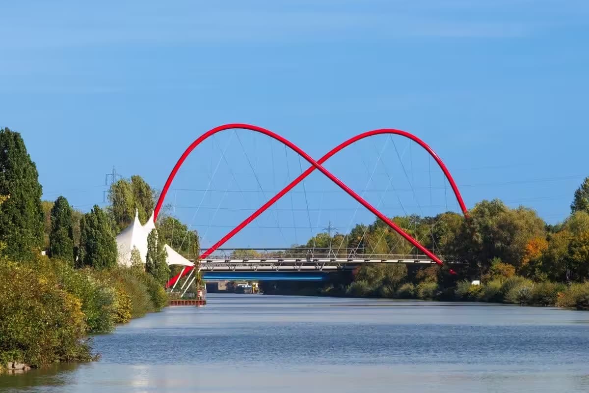 Rote Stahlbrücke über Kanal und Bäume entlang.
