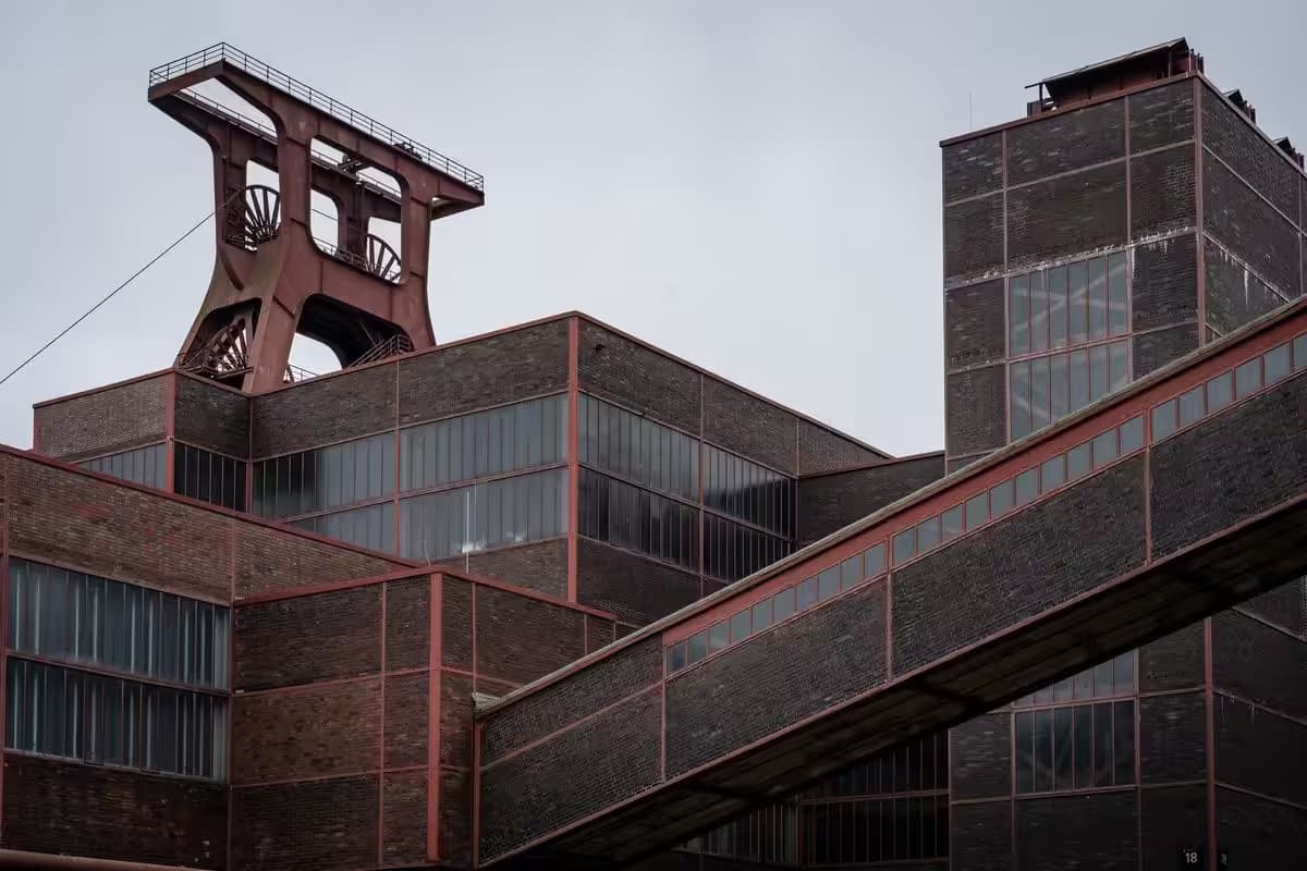 Industrielles Backsteingebäude mit Förderturm vor grauem Himmel.