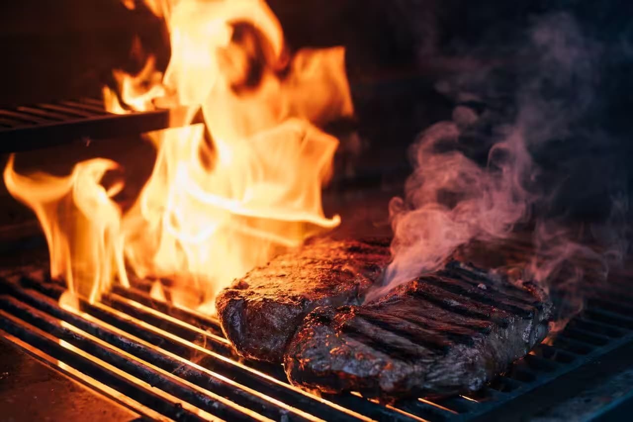 Gegrilltes Steak über offener Flamme auf Grillrost.