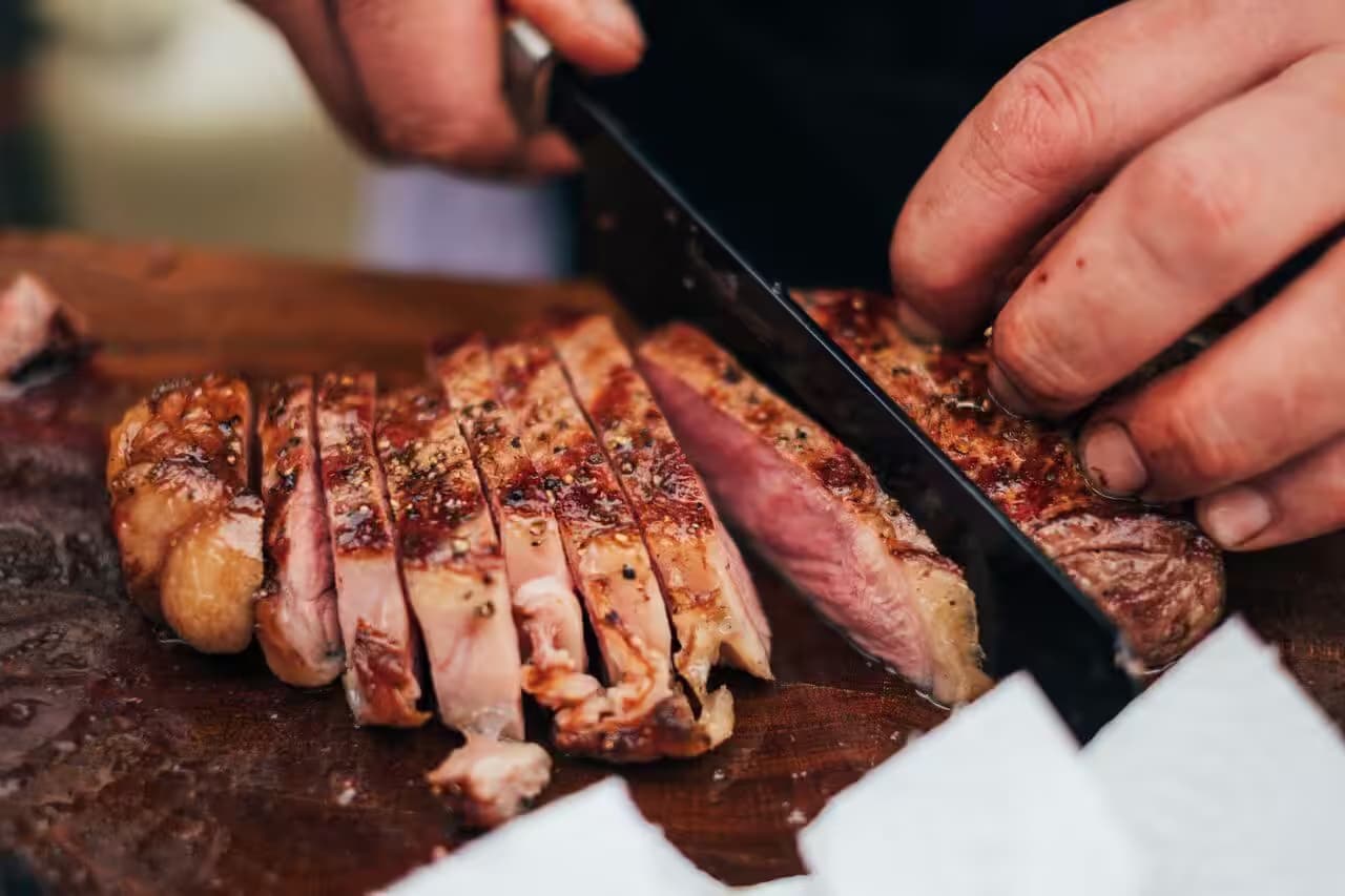 Person schneidet gegrilltes Steak auf Holzbrett