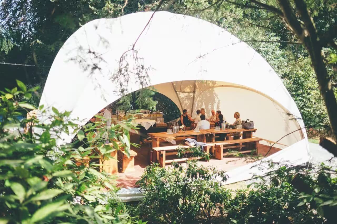Menschen sitzen unter Pavillon im Freien beim Essen.