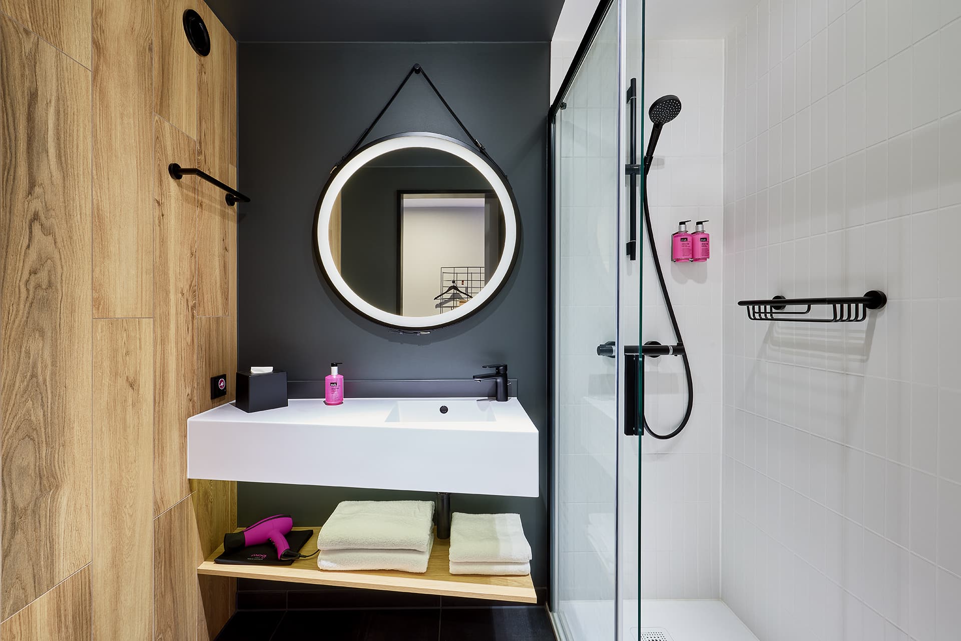Badezimmer im Moxy Hotel Karlsruhe mit Dusche und rundem Spiegel