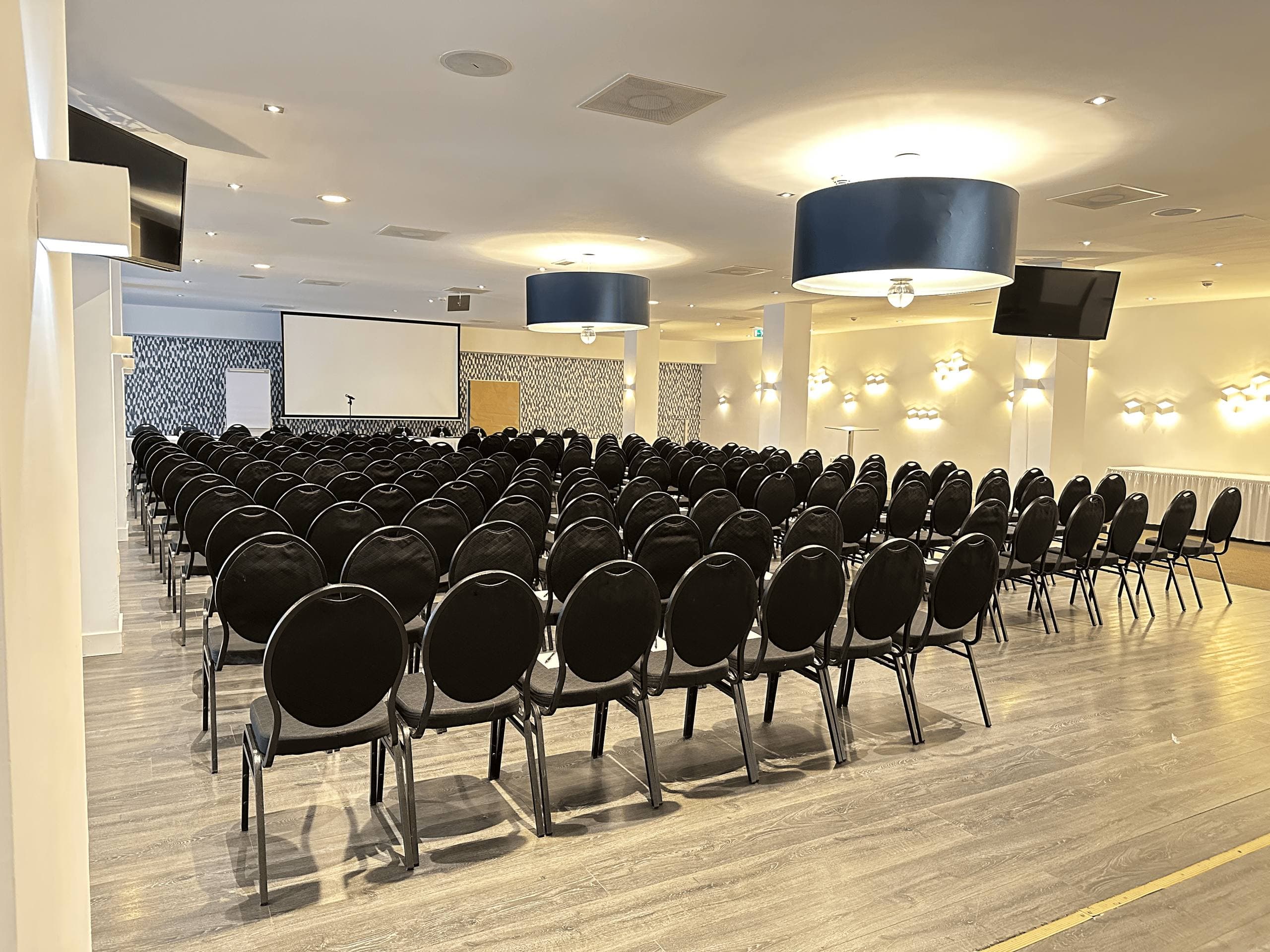 Event hall with theatre-style seating, projection screen and displays at the Van der Valk Hotel Moers