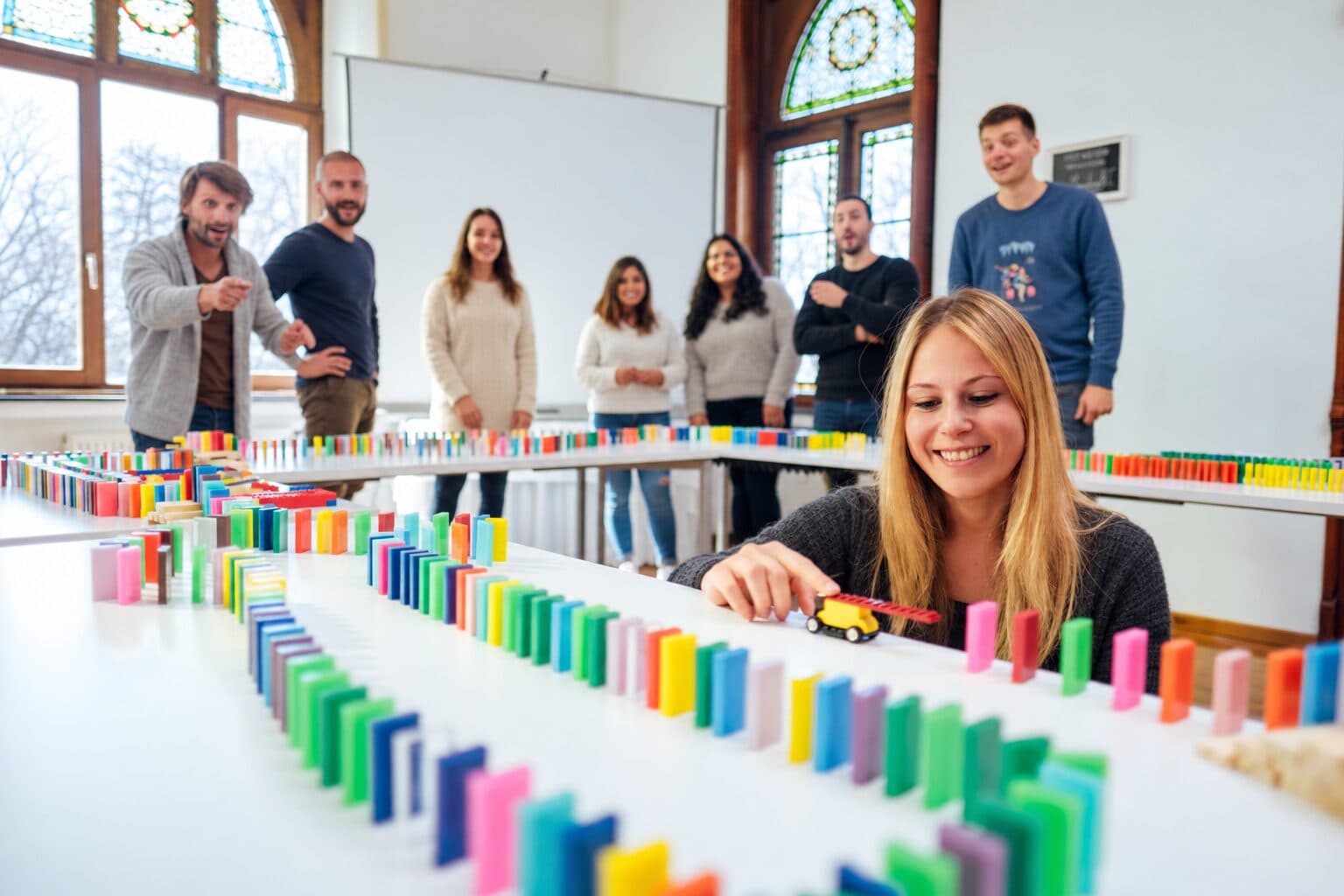 Teilnehmerin setzt ein LEGO-Fahrzeug in die Dominostrecke, das Team schaut zu