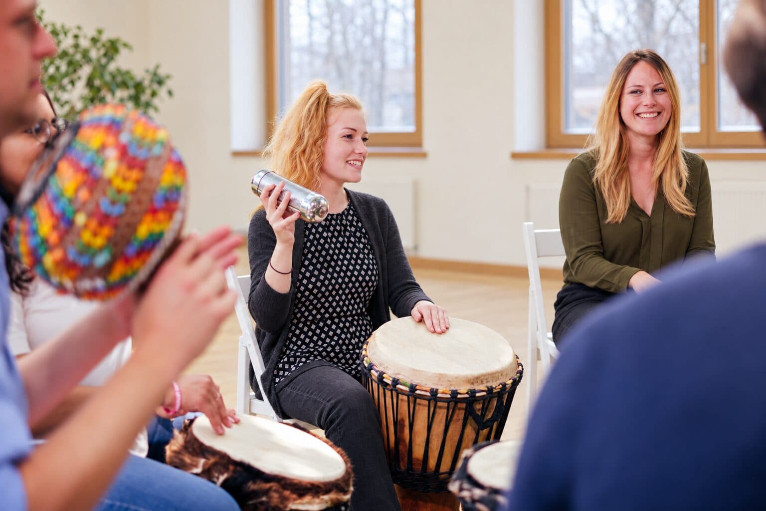 Teilnehmerin spielt Djembe und Shaker im Stuhlkreis