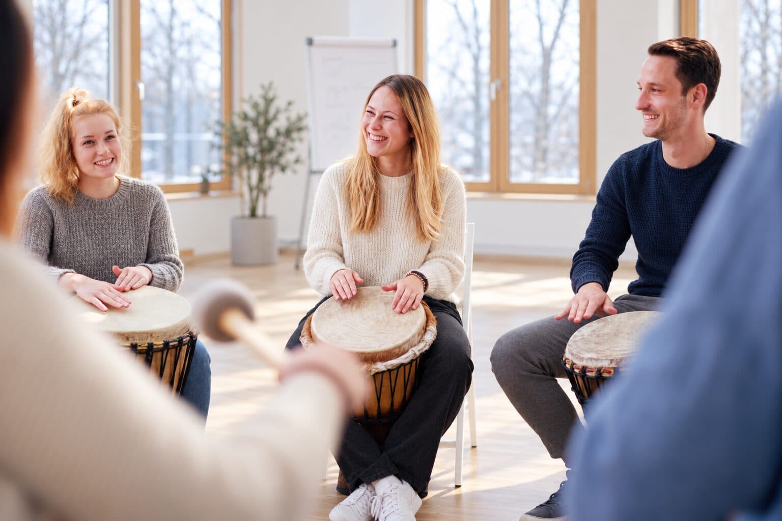 Drei Teilnehmende lachen beim gemeinsamen Trommeln auf Djemben