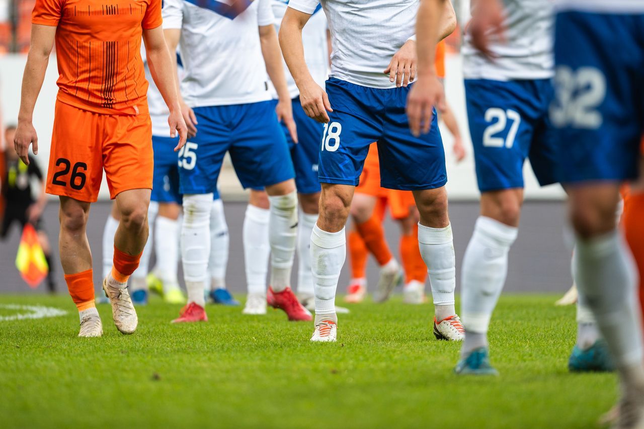 Fußballspieler in Orange und Weiß-Blau auf Spielfeld.