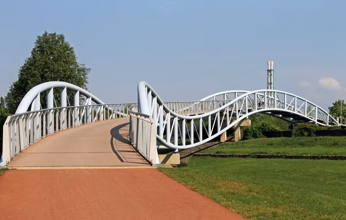 Moderne geschwungene Fußgängerbrücke über grüner Landschaft.