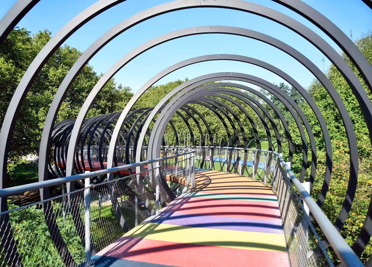 Bunte Fußgängerbrücke mit modernen Bögen im Park.