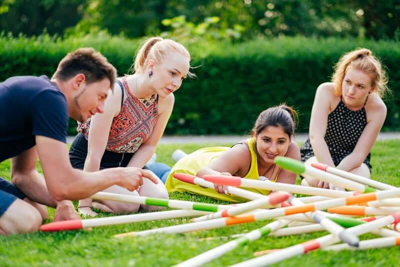 Gruppe spielt Mikado im Freien auf Rasen.