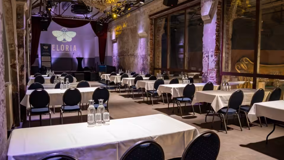 Veranstaltungsraum mit Tischen und Stühlen, Bühne vorne.