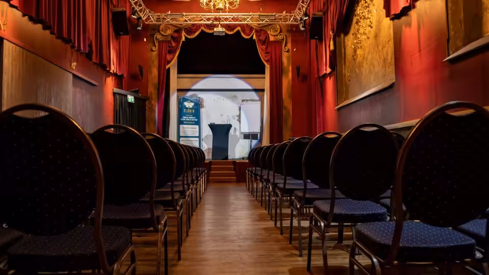 Leerer Theaterraum mit Bühne und Stühlen.