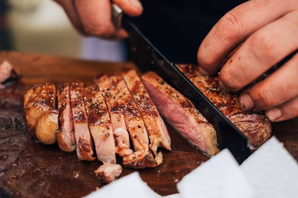 Person schneidet gegrilltes Steak auf Holzbrett