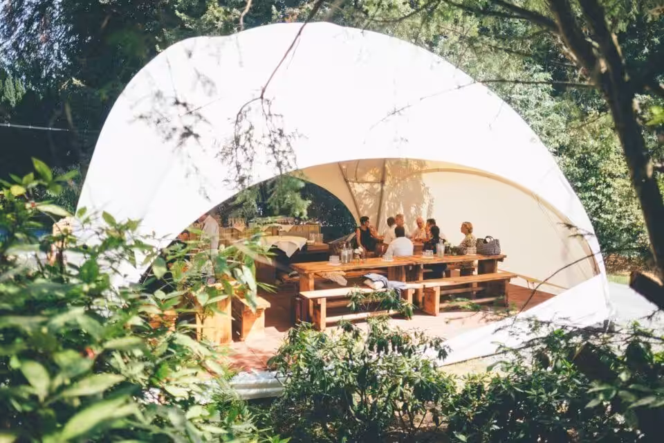Menschen sitzen unter Pavillon im Freien beim Essen.