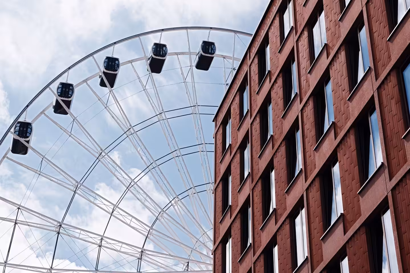 Riesenrad neben rotem Backsteingebäude und bewölktem Himmel.