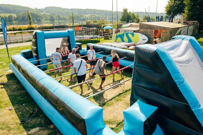 Menschen spielen auf einem aufblasbaren Tischfußballfeld im Freien.