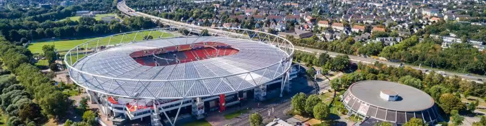 Luftaufnahme eines großen Fußballstadions, umgeben von Bäumen.